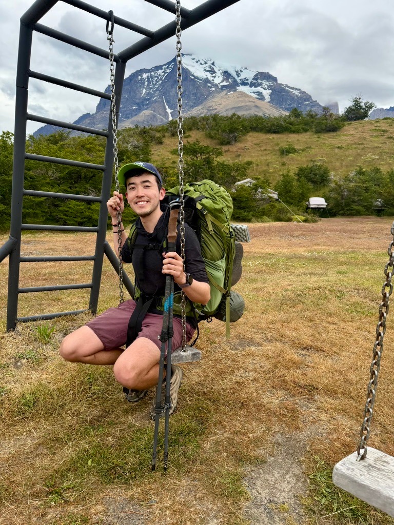Harvey Delaney on a swing with a backpack in front of mountains